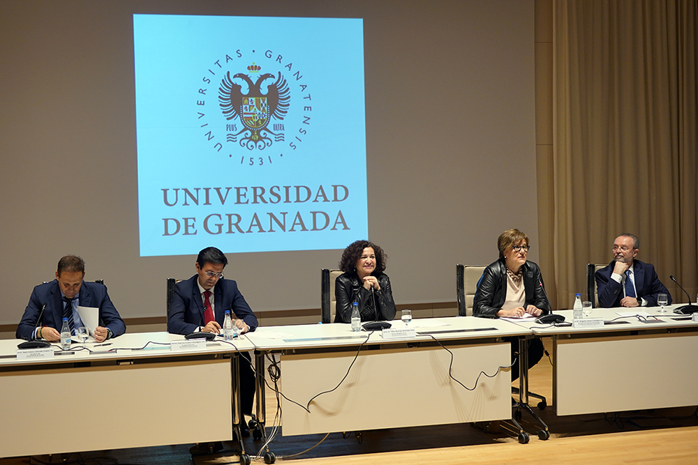 I Congreso de Investigación del PTS Bienvenida del congreso. Cinco personas (3 hombres y dos mujeres) están sentados tras unas mesas blancas. Tras ellos, el logo de la Universidad de ranada está proyectado en una pantalla.
